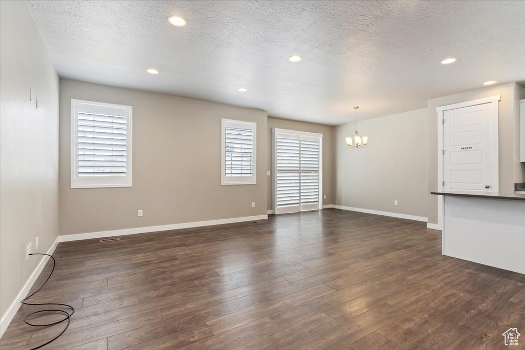 Unfurnished living room with a chandelier, dark wood finished floors, recessed lighting, and a textured ceiling