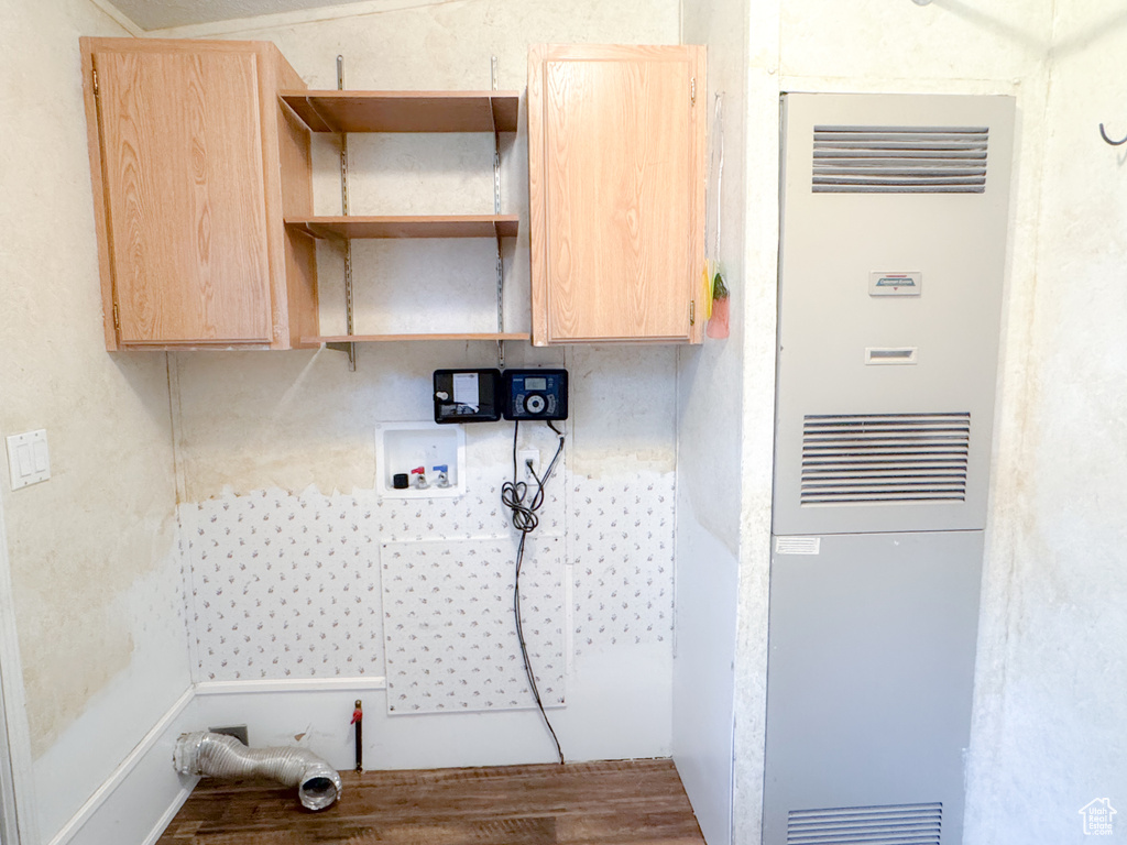 Laundry room featuring a heating unit, cabinet space, and wood finished floors