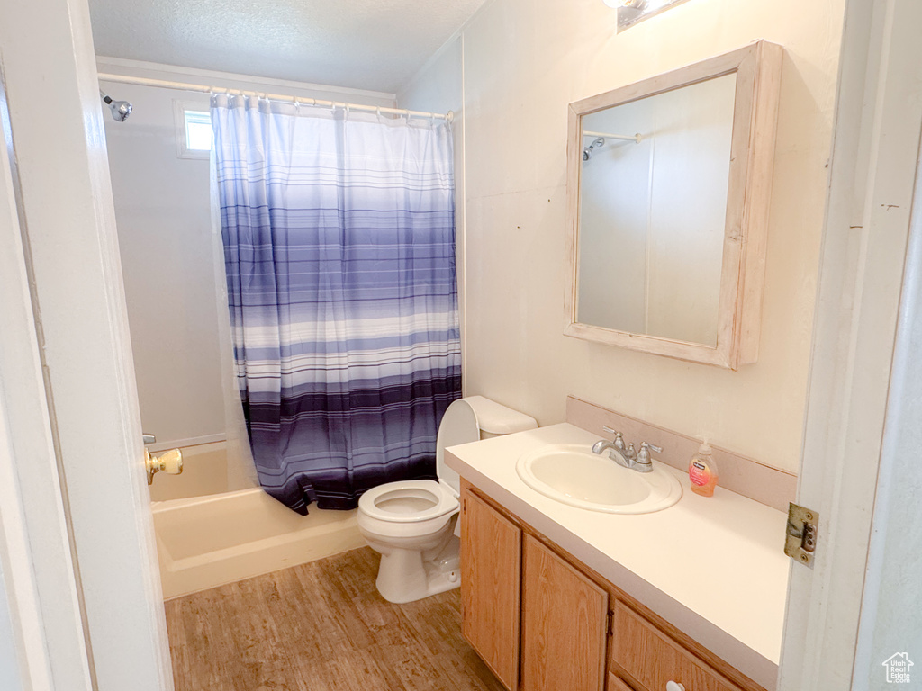 Bathroom featuring wood finished floors, vanity, shower / bath combination with curtain, and a textured ceiling