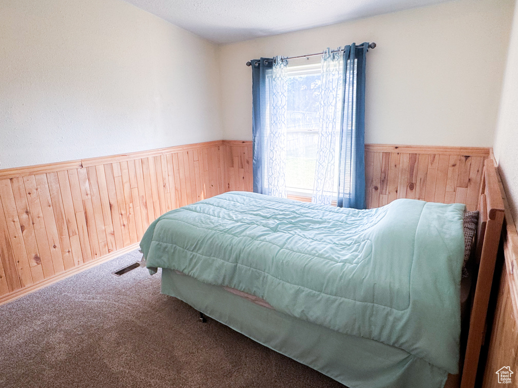 Bedroom with wooden walls, wainscoting, and carpet floors