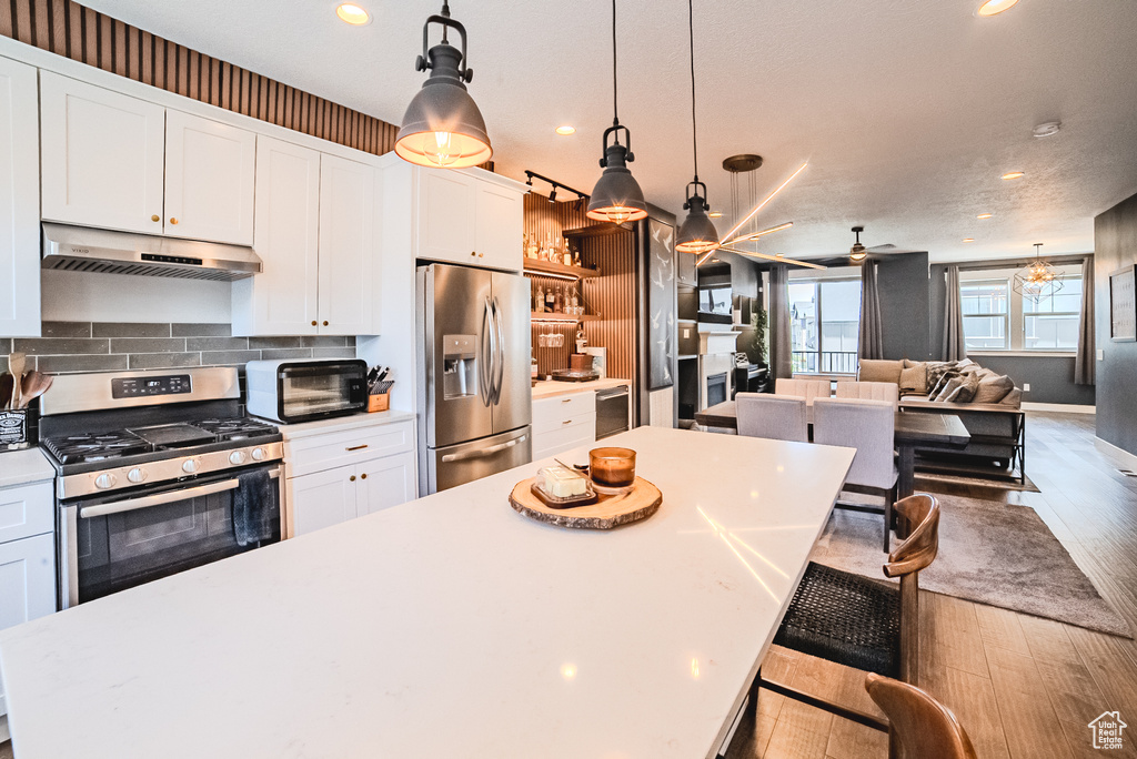 Kitchen featuring appliances with stainless steel finishes, under cabinet range hood, wood finished floors, open floor plan, and white cabinets
