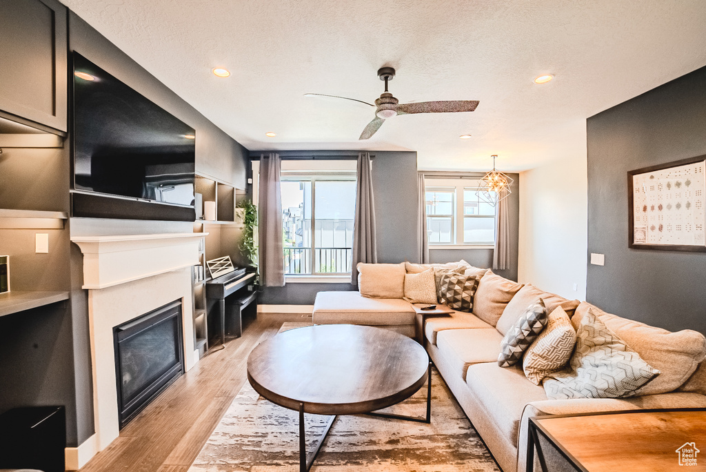 Living area featuring light wood-type flooring, ceiling fan, a glass covered fireplace, and recessed lighting