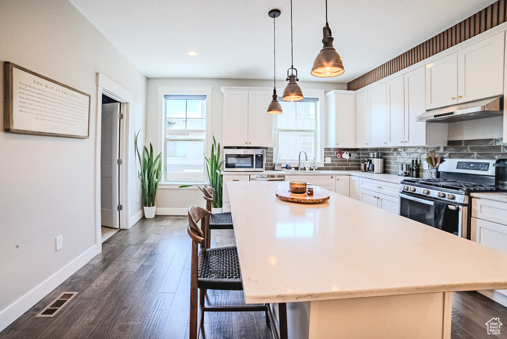Kitchen with under cabinet range hood, stainless steel appliances, a breakfast bar, light countertops, and recessed lighting