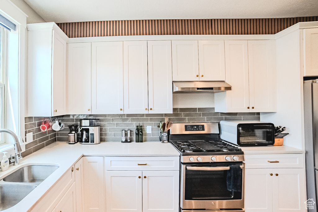 Kitchen featuring appliances with stainless steel finishes, under cabinet range hood, white cabinetry, and backsplash