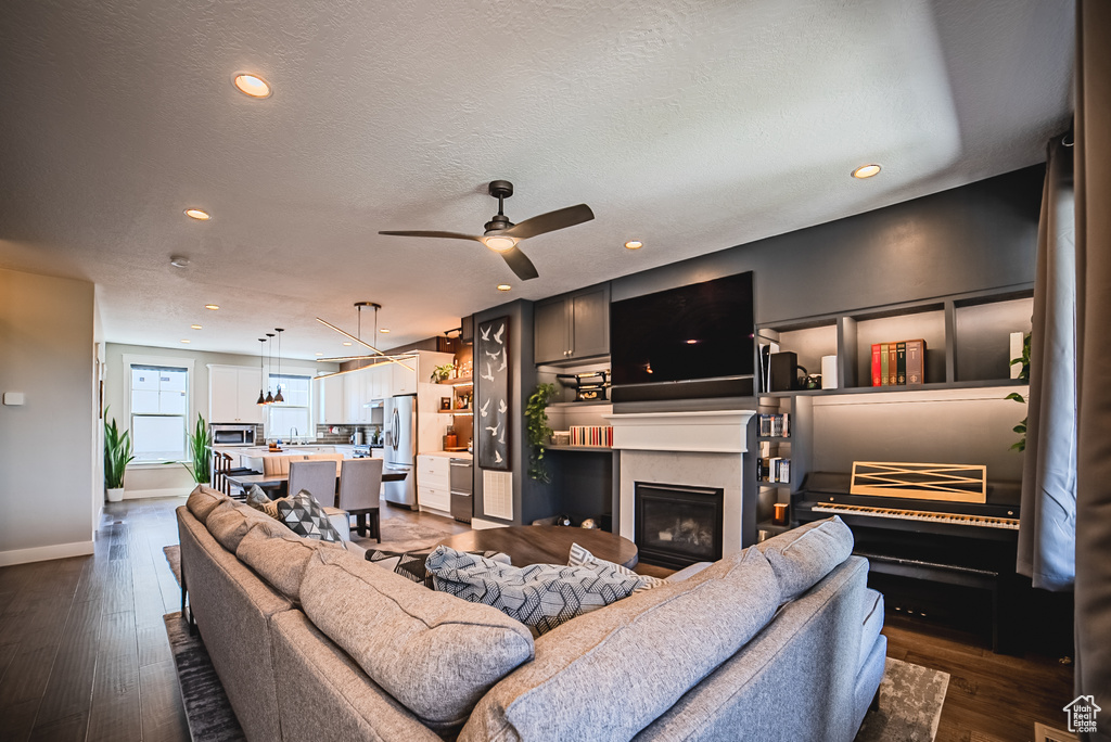 Living room featuring a glass covered fireplace, dark wood-style floors, a ceiling fan, recessed lighting, and a textured ceiling