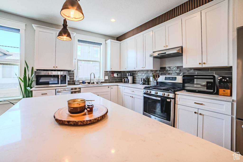 Kitchen featuring stainless steel appliances, under cabinet range hood, backsplash, white cabinets, and light countertops