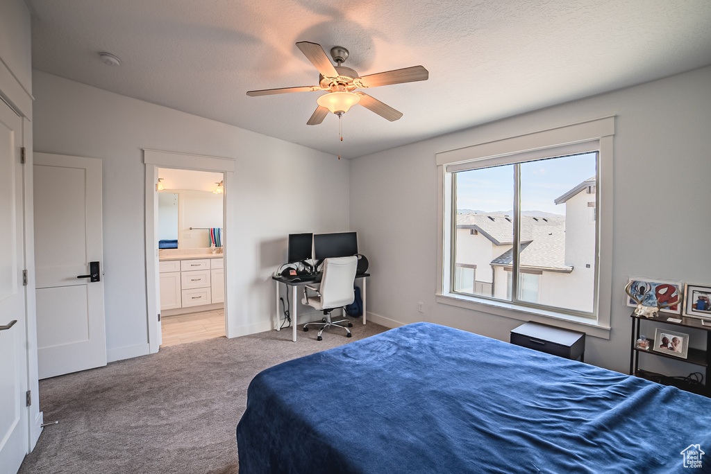 Bedroom featuring light colored carpet, ensuite bath, ceiling fan, and a desk