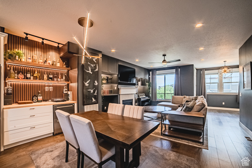 Dining room featuring a fireplace, a textured ceiling, wood finished floors, a ceiling fan, and recessed lighting
