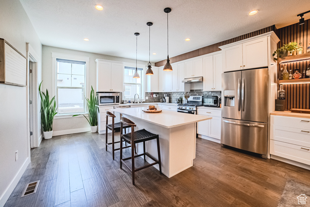 Kitchen featuring stainless steel appliances, under cabinet range hood, tasteful backsplash, white cabinets, and recessed lighting