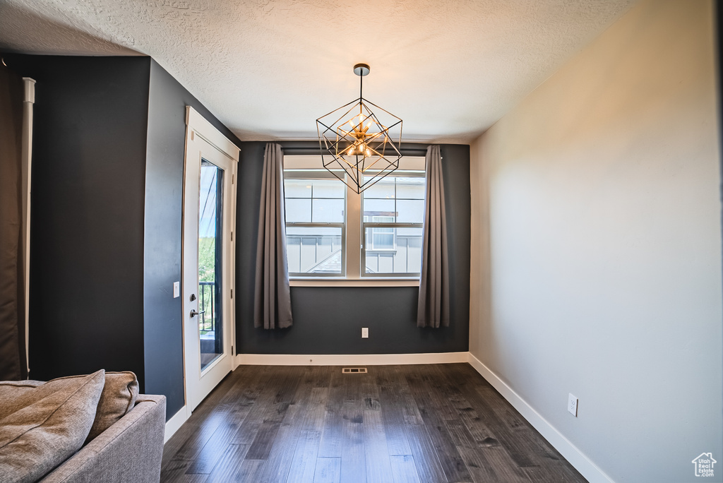 Unfurnished dining area featuring a chandelier, dark wood-style flooring, and a textured ceiling