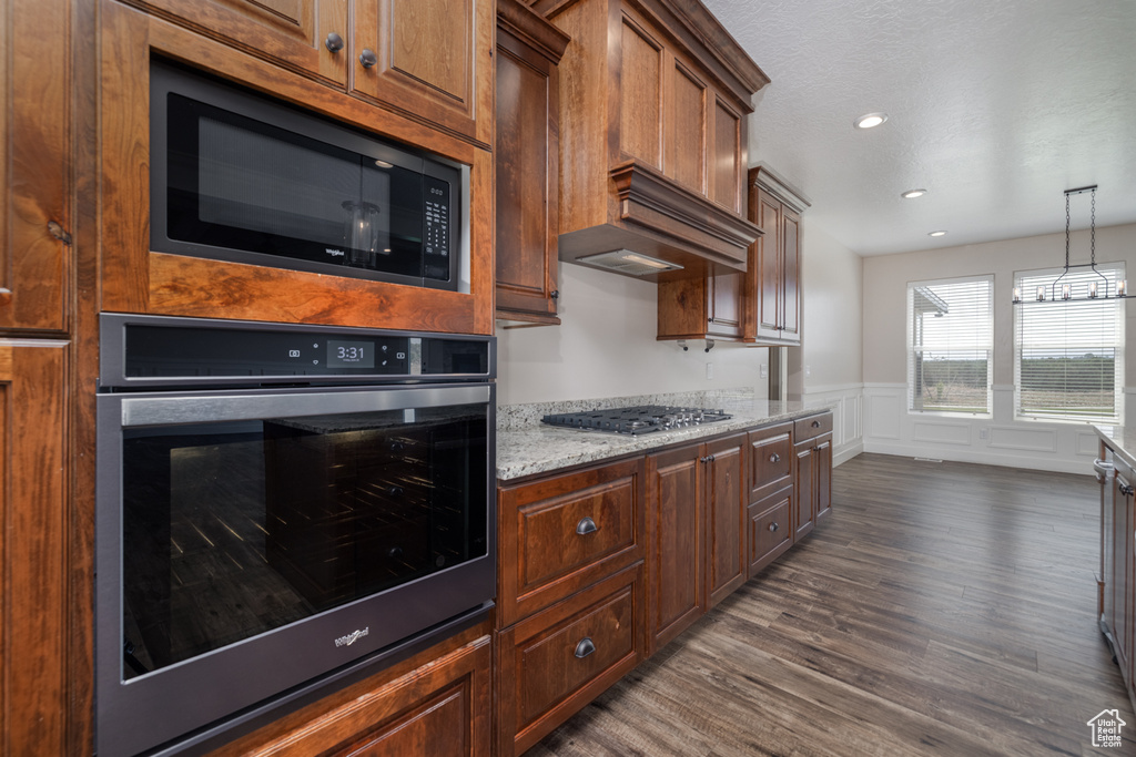 Kitchen featuring stainless steel appliances, dark wood finished floors, wainscoting, light stone counters, and pendant lighting