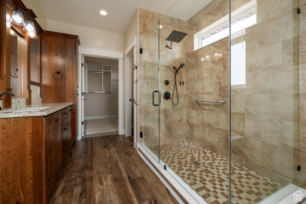 Full bath with wood finished floors, a shower stall, vanity, a walk in closet, and recessed lighting