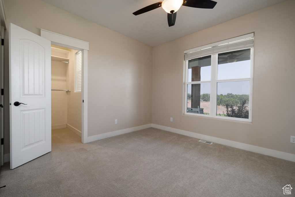 Unfurnished bedroom featuring light carpet, a walk in closet, a ceiling fan, and a closet