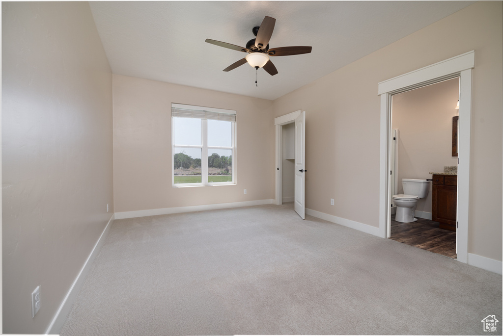 Unfurnished bedroom featuring light colored carpet, ensuite bathroom, and ceiling fan