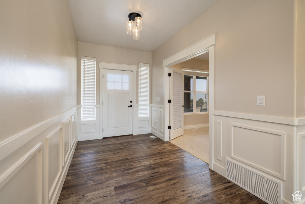 Entrance foyer with dark wood-style flooring, a wainscoted wall, and a decorative wall