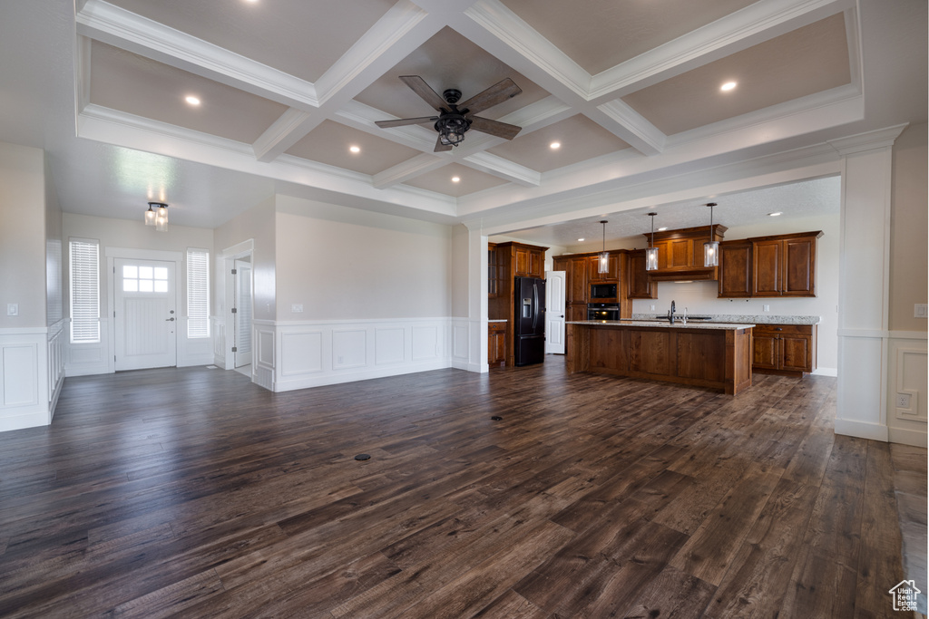 Unfurnished living room with a decorative wall, coffered ceiling, beamed ceiling, ceiling fan, and dark wood-style floors