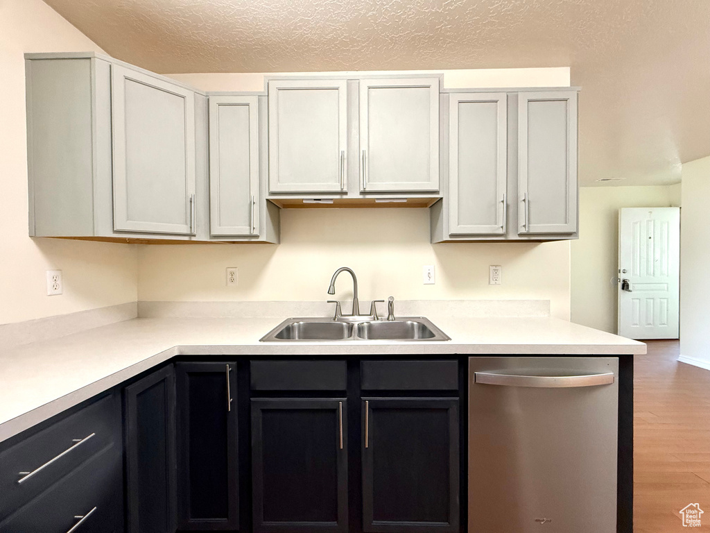 Kitchen with stainless steel dishwasher, wood finished floors, light countertops, and a textured ceiling