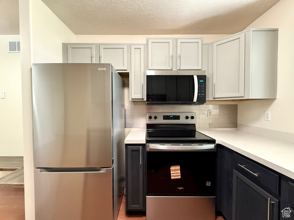 Kitchen featuring appliances with stainless steel finishes, light countertops, backsplash, a textured ceiling, and light wood-style floors