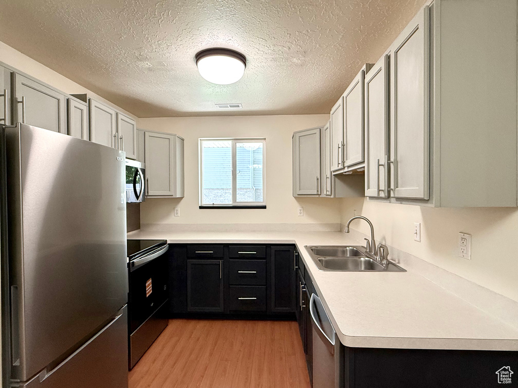 Kitchen featuring stainless steel appliances, light wood-type flooring, a textured ceiling, and light countertops