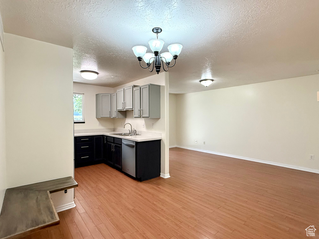 Kitchen featuring dishwasher, a textured ceiling, a chandelier, light wood finished floors, and light countertops