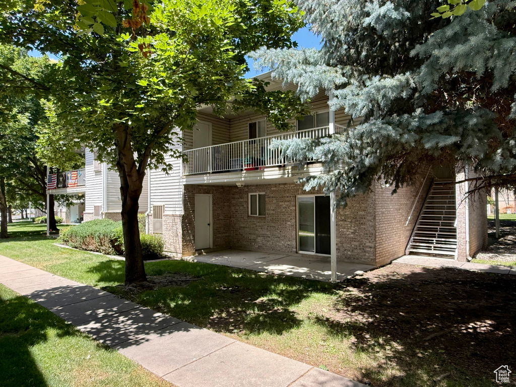 Back of property featuring a balcony, a patio area, brick siding, a yard, and stairway