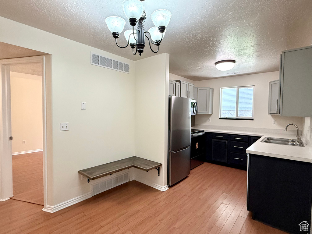 Kitchen featuring stainless steel appliances, a textured ceiling, light wood finished floors, light countertops, and a chandelier