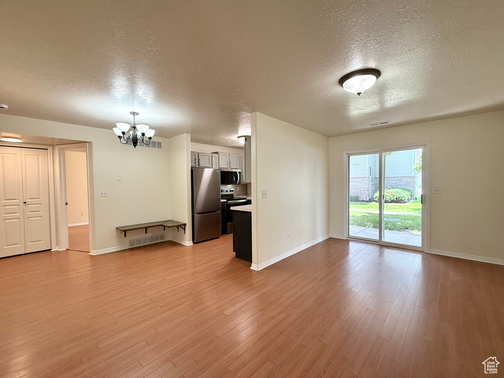 Unfurnished living room with a textured ceiling, a chandelier, and wood finished floors