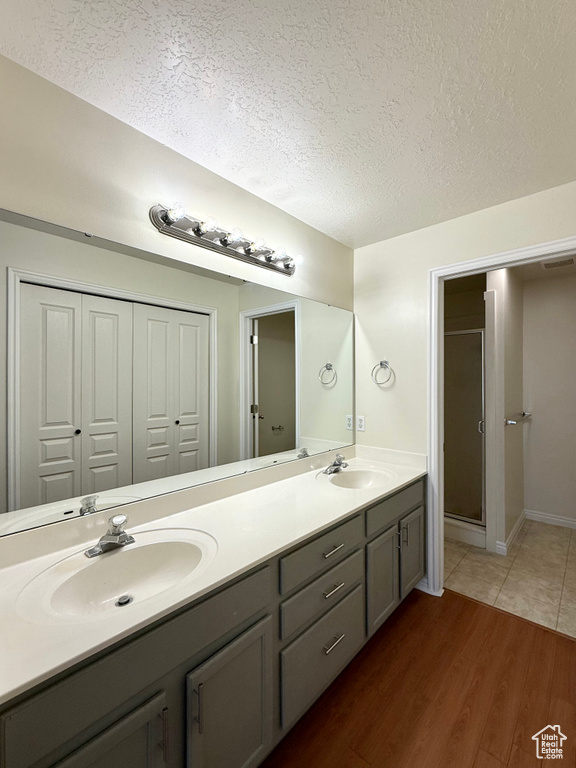 Bathroom with a textured ceiling, double vanity, wood finished floors, and a shower stall