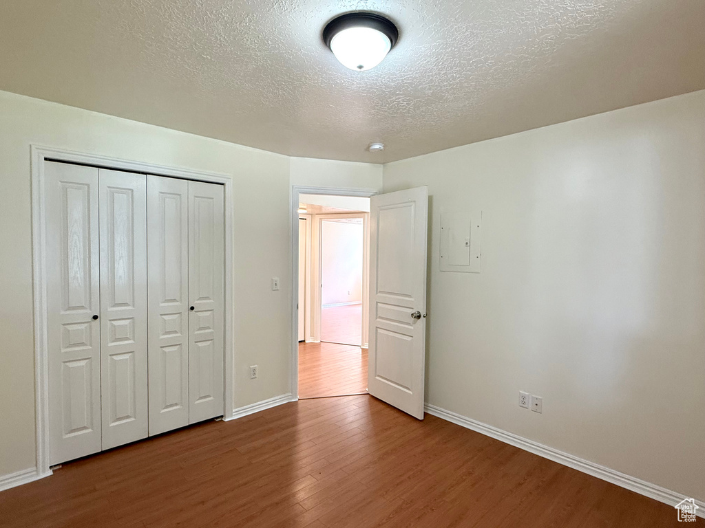 Unfurnished bedroom with a textured ceiling, wood finished floors, a closet, and electric panel