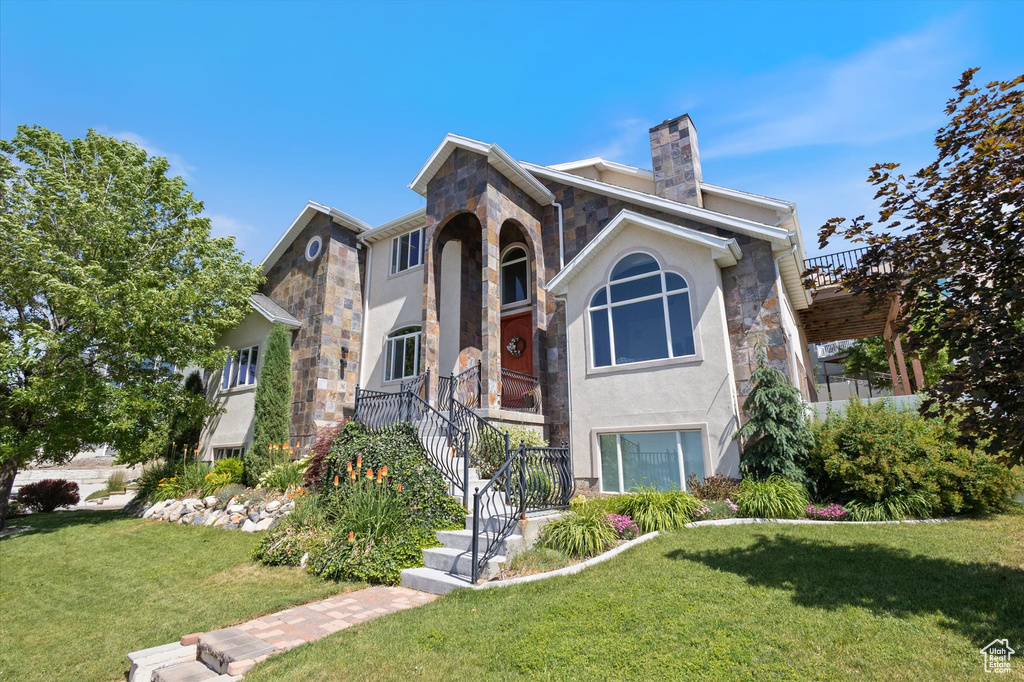 View of front of home featuring stone siding, stucco siding, a front lawn, a chimney, and stairway