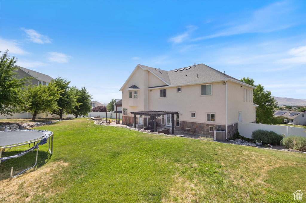 Rear view of house featuring a trampoline, a patio area, a pergola, a fenced backyard, and stone siding