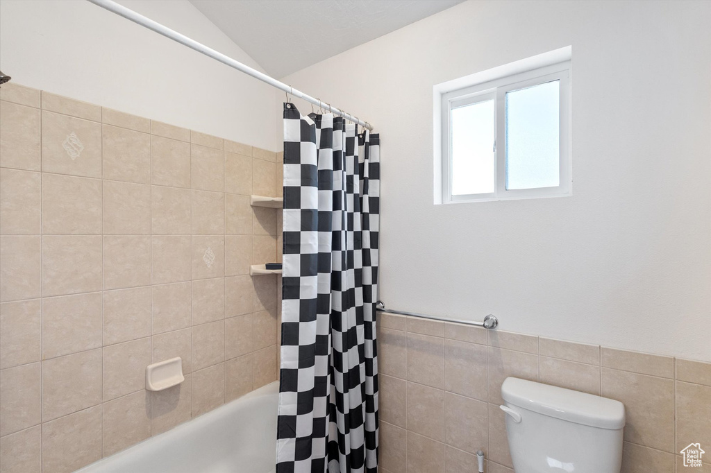 Bathroom with tile walls, shower / bath combo with shower curtain, and a wainscoted wall