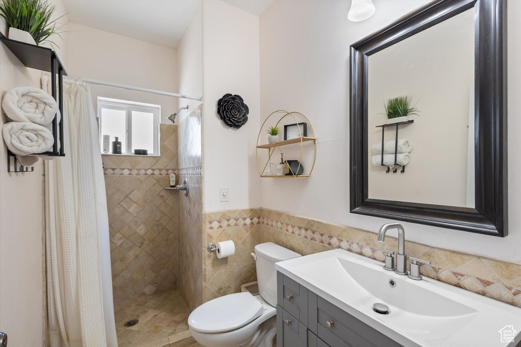 Bathroom with vanity, a shower stall, wainscoting, and tile walls