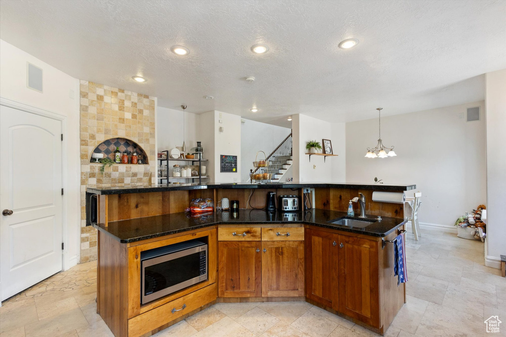 Kitchen with stainless steel microwave, a large island with sink, a chandelier, dark stone counters, and a textured ceiling