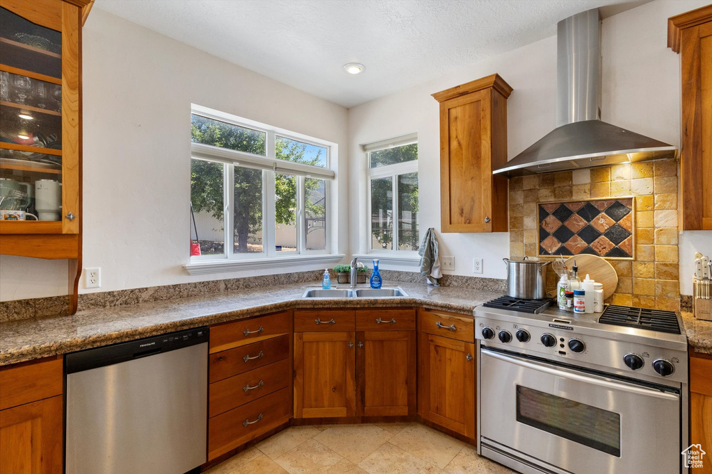 Kitchen featuring appliances with stainless steel finishes, wall chimney exhaust hood, brown cabinets, decorative backsplash, and recessed lighting