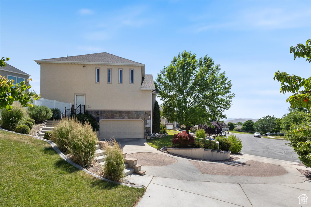 View of side of property with driveway, stucco siding, stone siding, a garage, and a lawn