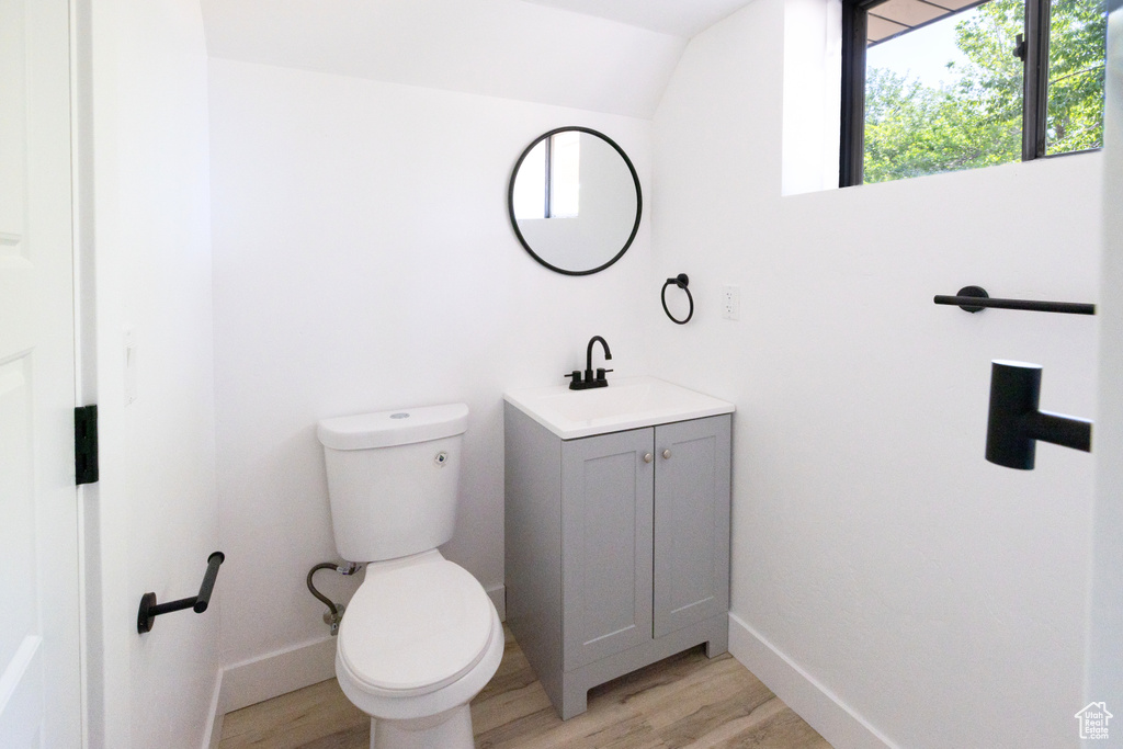 Half bath with vanity, wood finished floors, and lofted ceiling