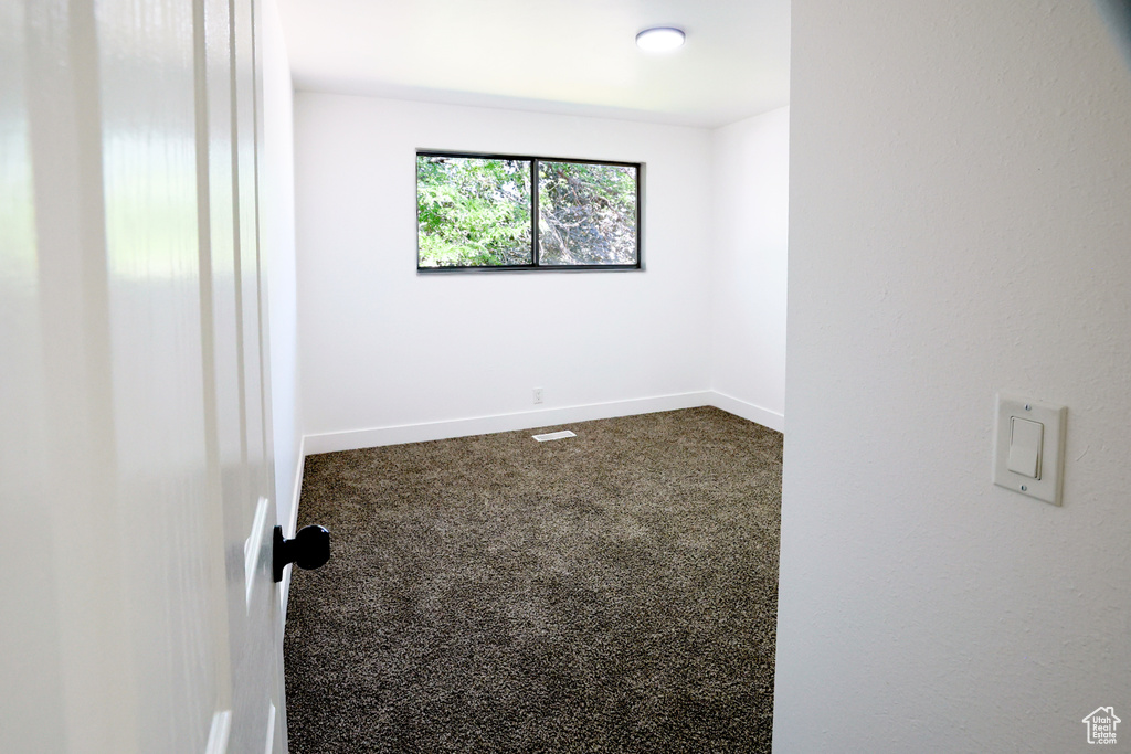 Unfurnished room featuring dark carpet and baseboards