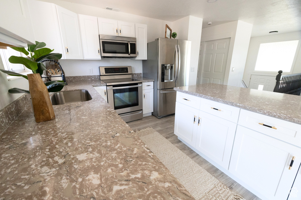 Kitchen featuring stainless steel appliances, light stone countertops, light wood finished floors, and white cabinetry