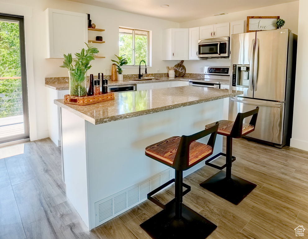 Kitchen with appliances with stainless steel finishes, a breakfast bar area, white cabinetry, open shelves, and light stone counters