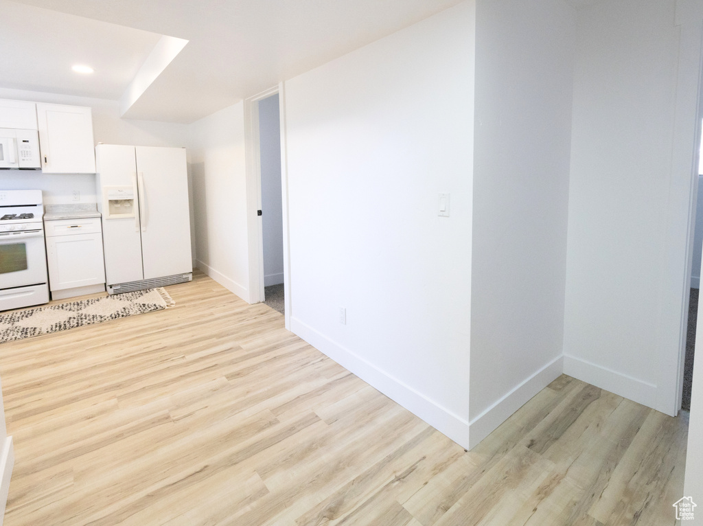 Kitchen featuring white appliances, light wood-type flooring, light countertops, white cabinetry, and recessed lighting