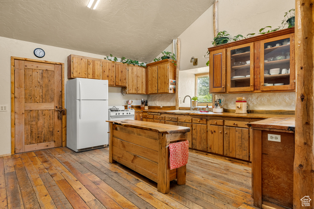 Kitchen featuring white appliances, vaulted ceiling, light wood-type flooring, brown cabinetry, and tile countertops