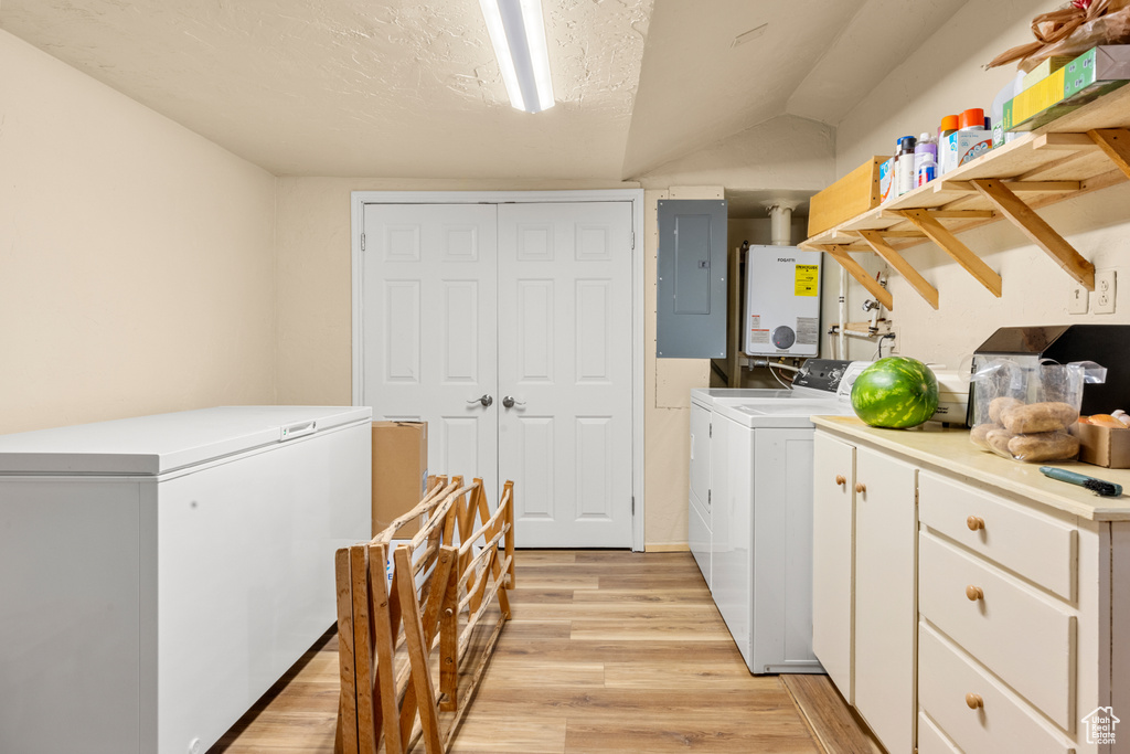 Laundry room featuring electric panel, washer and dryer, water heater, light wood-style flooring, and cabinet space