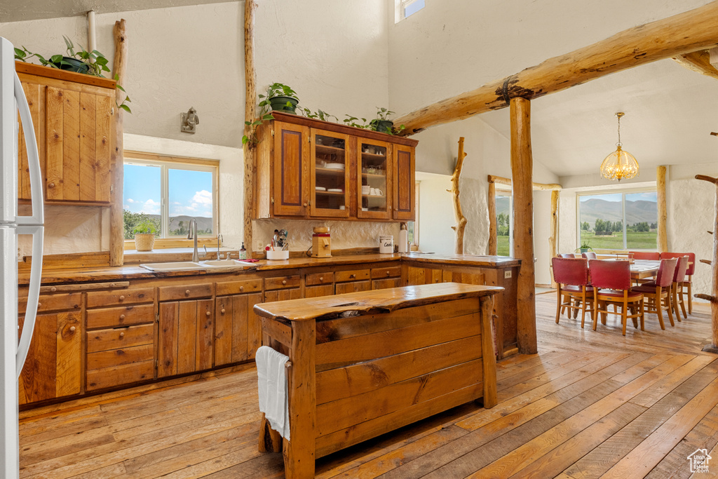Kitchen with brown cabinetry, light wood finished floors, a chandelier, freestanding refrigerator, and beamed ceiling