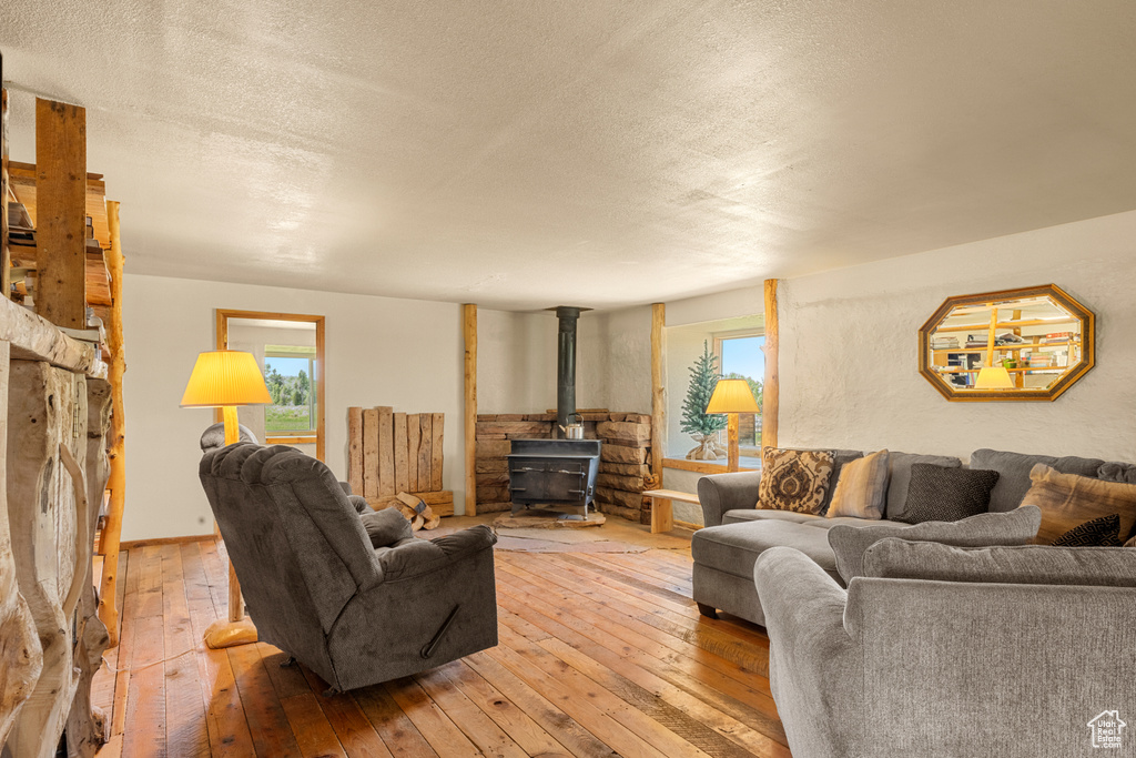 Living room featuring a wood stove, wood-type flooring, healthy amount of natural light, and a textured ceiling