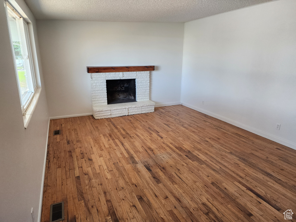Unfurnished living room featuring hardwood / wood-style floors, a brick fireplace, and a textured ceiling