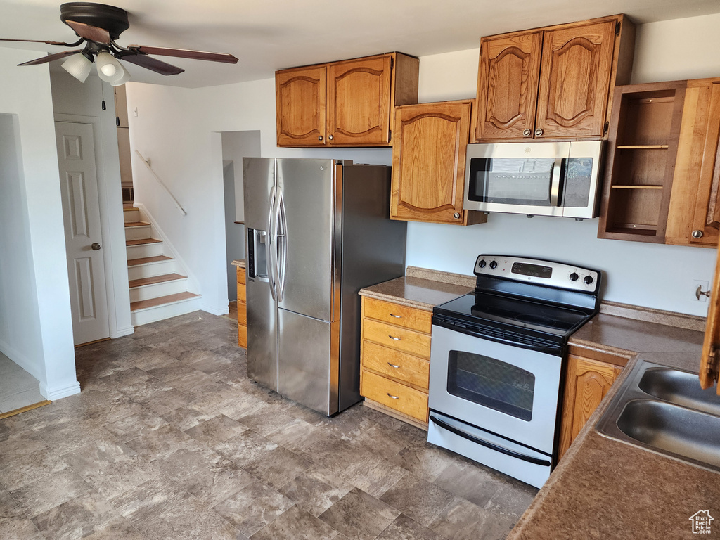 Kitchen featuring appliances with stainless steel finishes, ceiling fan, brown cabinets, and dark countertops