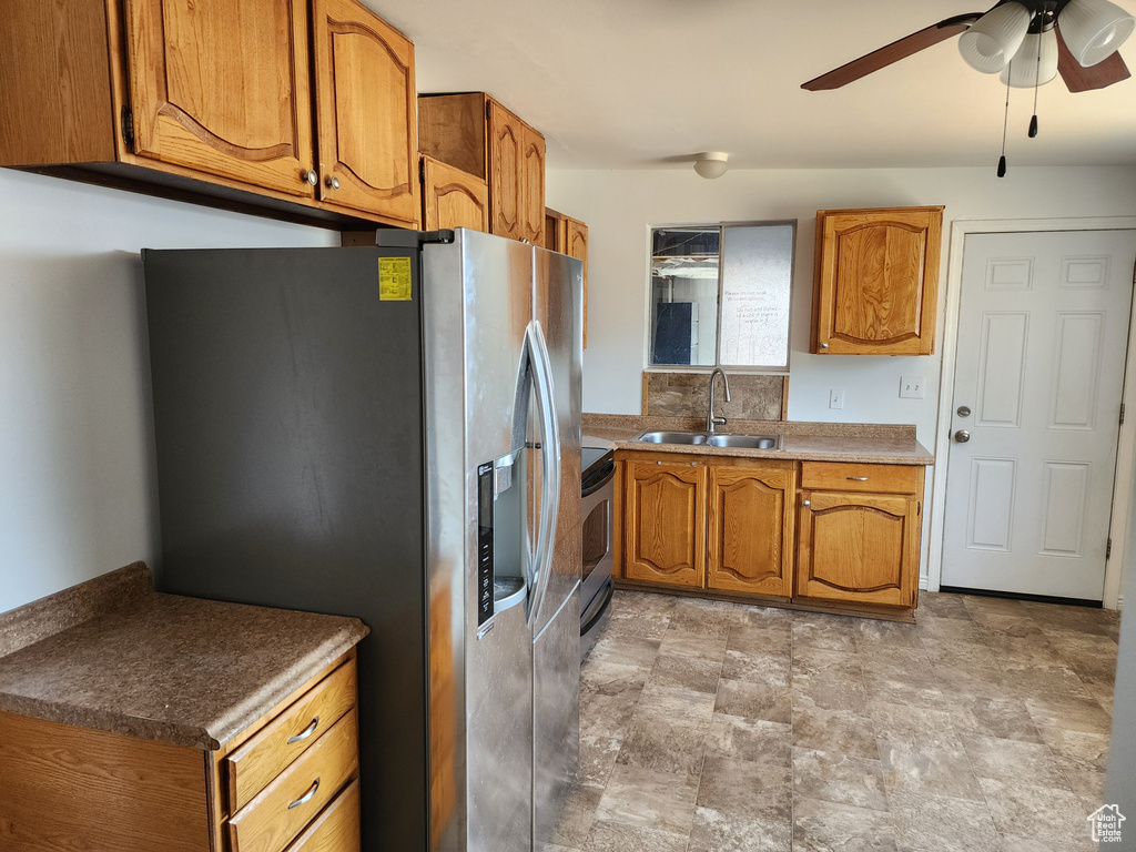 Kitchen featuring appliances with stainless steel finishes, brown cabinets, a ceiling fan, and stone finish floors