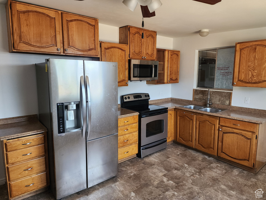 Kitchen with stainless steel appliances, brown cabinetry, ceiling fan, dark countertops, and stone finish floors