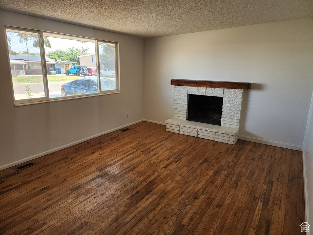 Unfurnished living room featuring dark wood-style floors, a textured ceiling, and a brick fireplace